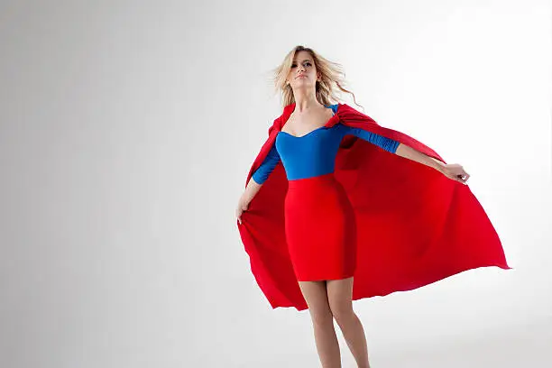 Superhero Woman. Young and beautiful blonde in the image of a superheroine in a red Cape growing