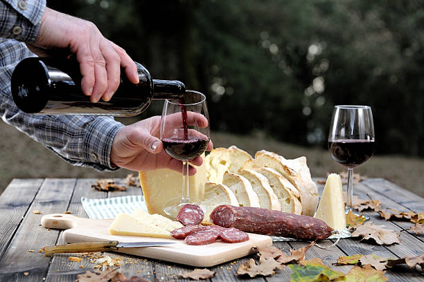 Hands that shed the wine into the chalice while eating in the countryside with bread, cheese and sausage.