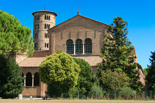 Basilica of Sant'Apollinare in Classe near Ravenna, Italy. This brick structure was erected at the beginning of 6th century. Green trees, belltower, cross and vivid blue clear sky are in the image.