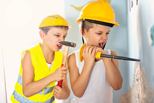 Two little manual workers renovating their room. Boys aged 7 are tearing out plaster from the walls using hammer and chisel.