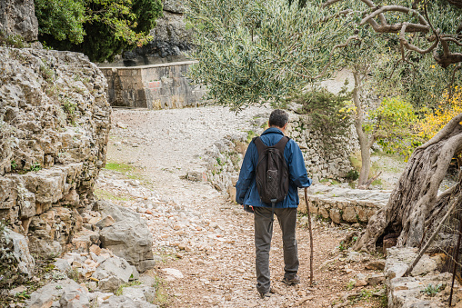 Senior Caucasian male hiker walking towards the Blaca Monastery in the forest on the Brač island in Croatia, Mediterranean, Europe. Sunny autumnal day. Rear view. Beautiful tree. Nikon D800, full frame, XXXL.