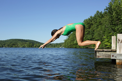 Girl dives into a calm summer lake in the countryside of Vermont