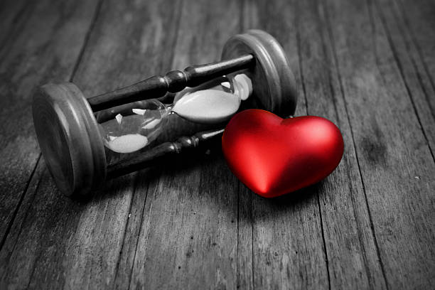 Close up of Red heart and hourglass on wood background, vignette effect concept. Time concept and copy space, vintage style, black and white tone.