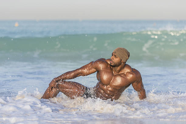 istock Dark Muscular man laying on beach splashed by ocean waves 637628162