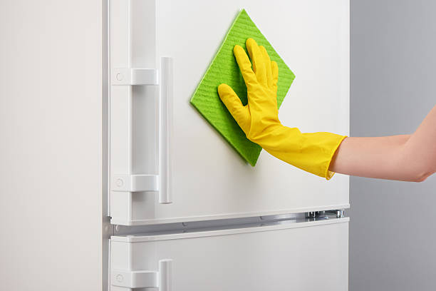 istock Hand in yellow glove cleaning white refrigerator with green rag 637638596