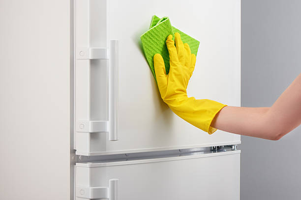 istock Hand in yellow glove cleaning white refrigerator with green rag 637639434