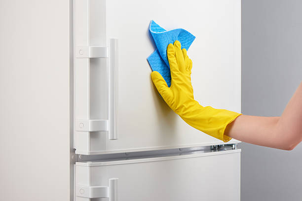 istock Hand in yellow glove cleaning white refrigerator with blue rag 637639502