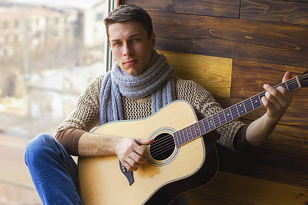 istock guitarist young guy in jeans with a guitar sitting 637643842