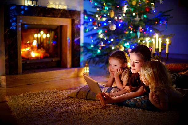 istock Mother and daughters using tablet by a fireplace on Christmas 637645440