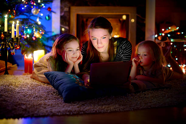 mutter und tochter mit tablet um einen kamin auf weihnachten - sibling baby three people baby girls stock-fotos und bilder