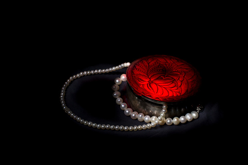 An old engraved silver box with red illuminated lid and pearl jewels on black tissue. Light painting with LED flashlights.