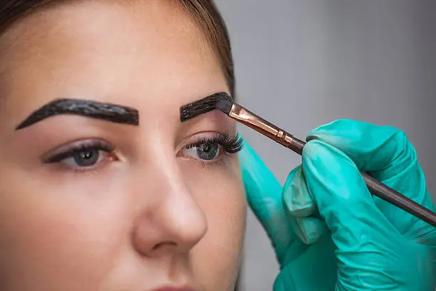 Photo of makeup artist applies paint henna on eyebrows.