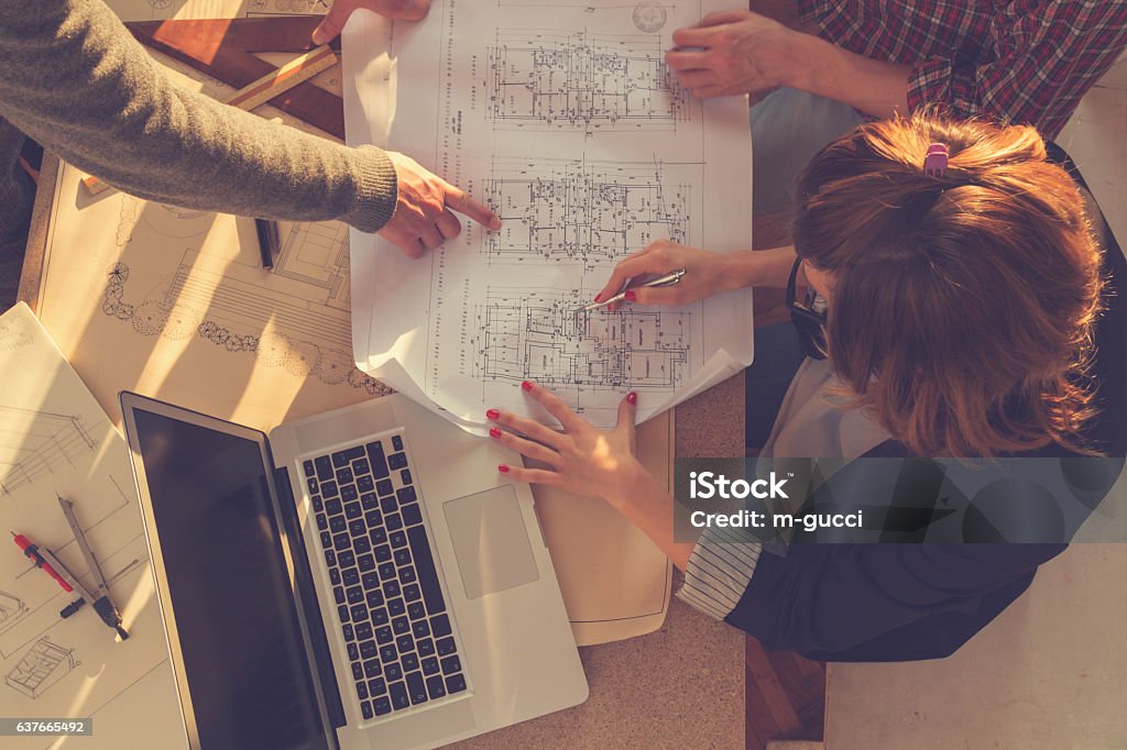 Group of people/architects discussing business plans. Group of people discussing business plans, with lap-tops, plans in a room lit by natural sunlight. Blueprint Stock Photo