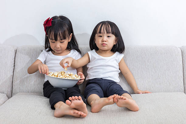 istock Asian Chinese little sisters eating popcorn on the sofa 637670944