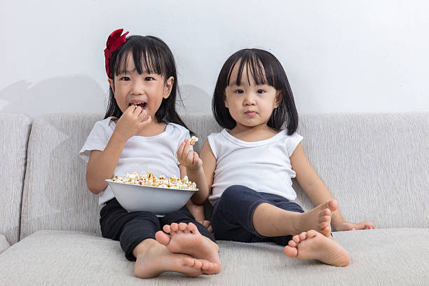 istock Happy Asian Chinese little sisters eating popcorn on the sofa 637671180