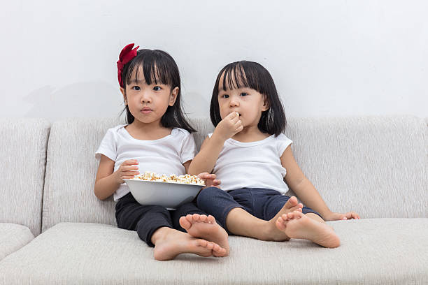 istock Asian Chinese little sisters eating popcorn on the sofa 637671374