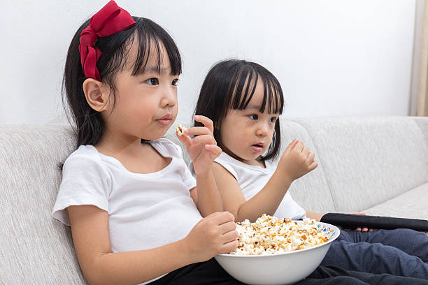 istock Asian Chinese little sisters eating popcorn on the sofa 637671758
