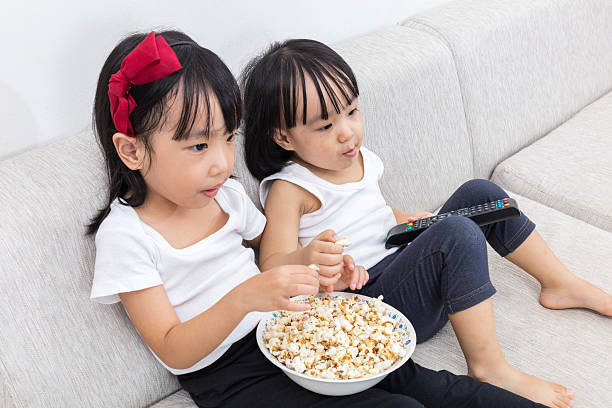 istock Asian Chinese little sisters eating popcorn on the sofa 637673868
