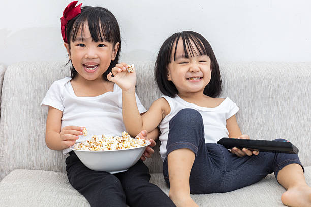 istock Happy Asian Chinese little sisters eating popcorn on the sofa 637674112