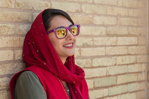 Young iranian woman with a typcial simple headscarf (hijab or rousari) and sunglasses. In the mirror of her sunglasses the Si-o-seh pol bridge in Isfahan is visible.