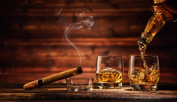 Glasses of whiskey with ice cubes served on wood Pouring whiskey from bottle to two glasses with ice cubes, served on wooden planks. Vintage countertop with highlight and a glass of hard liquor cigar photos stock pictures, royalty-free photos & images