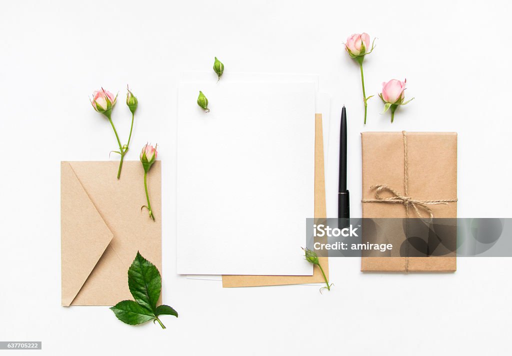 Letter, envelope and gift  with pink roses. Holiday flat lay Letter, envelope and a present in eco paper on white background. Wedding invitation cards or love letter with pink roses. Valentine's day or other holiday concept, top view, flat lay, overhead view Wedding Stock Photo