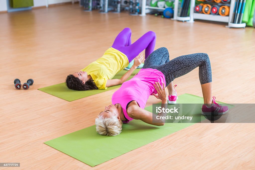 Women training their glutes by doing bridging exercise on mats Women training their glutes by doing bridging exercise on mats in gymnasium. Exercising Stock Photo