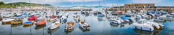 Families of holiday makers on the historic Cobb overlooking Lyme Regis and the boats moored in its tranquil harbour.