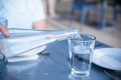 Close up view of a hand Pouring Distilled water into a clear glass at a restaurant. A healthy choice