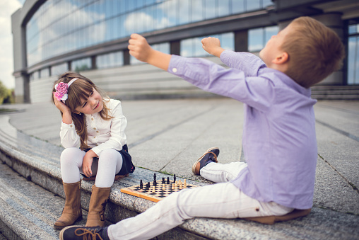 Disappointed business girl looking at her friend who is celebrating after winning in chess game. Focus is on girl.