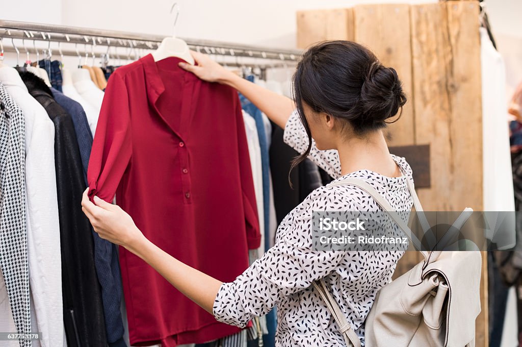 Woman at clothing store Woman choosing blouse from new collection of clothes in a boutique. Beautiful woman choosing clothes in a clothing shop. Rear view of girl doing shopping. Clothing Stock Photo