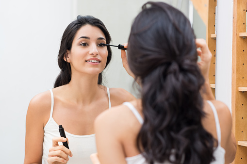 Woman applying black mascara on eyelashes with makeup brush. Young beautiful woman applying mascara makeup on eyes at bathroom. Beautiful brunette girl applying makeup on eyes in the morning time.