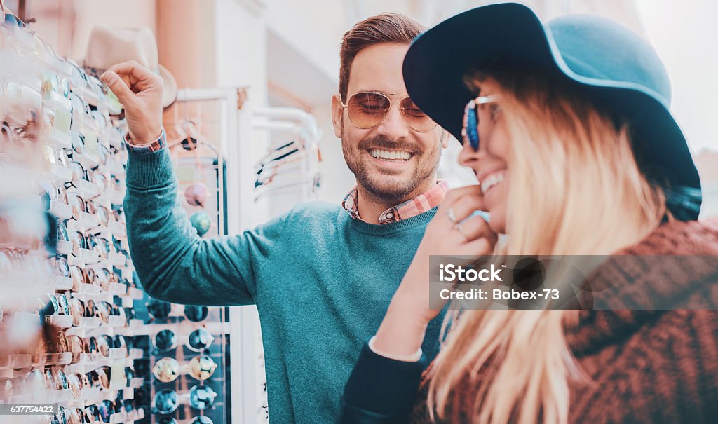 Young smiling couple shopping together Handsome young couple buying sun glasses at street vendor. Consumerism, shopping, lifestyle concept Shopping Stock Photo