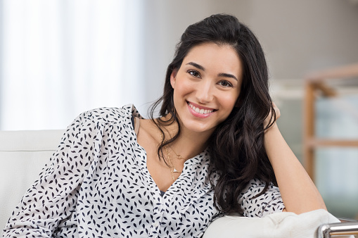 Closeup of a smiling young woman looking at camera. Portrait of happy brunette girl smiling at home. Relaxed woman at home smiling.