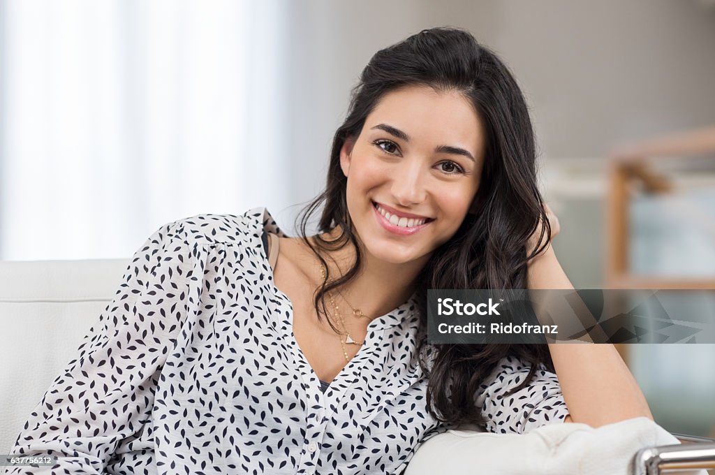 Happy young woman Closeup of a smiling young woman looking at camera. Portrait of happy brunette girl smiling at home. Relaxed woman at home smiling. Women Stock Photo