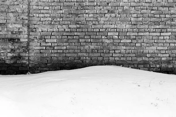 Weathered brick wall and snow inblack and white. Abstract seasonal background.
