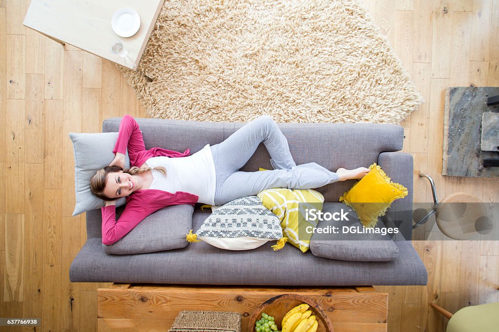 Woman Relaxing on Sofa Beautiful woman is lying on the sofa in the living room of her home. She is smiling at the camera which is directly above. Sofa Stock Photo