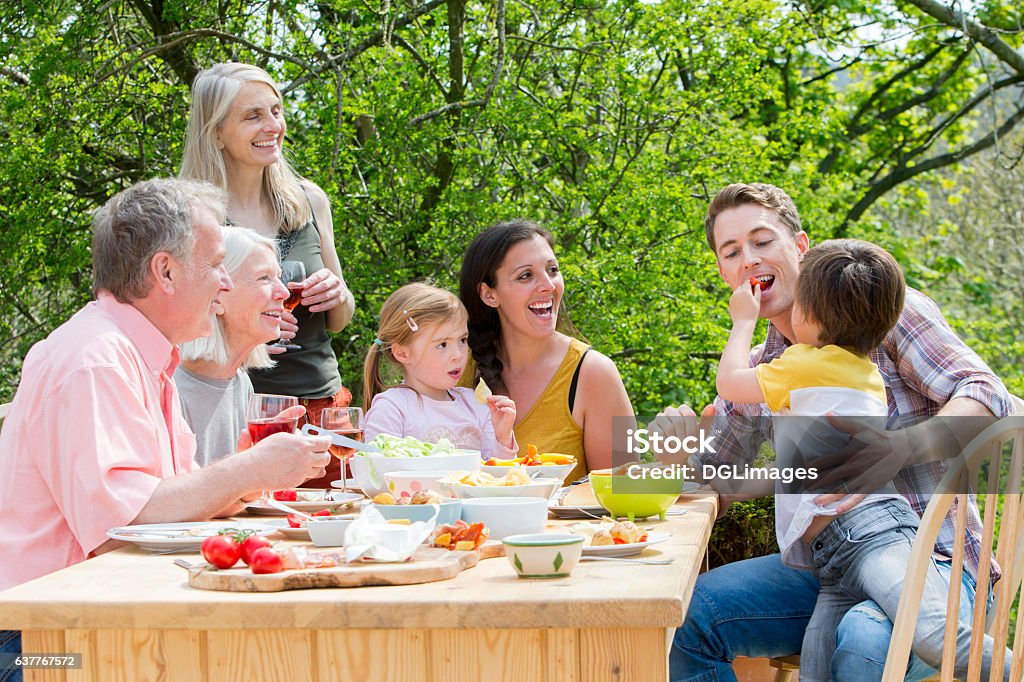 You Need To Eat Vegetables Too! Three generation family having a garden party in the summer. Everyone is laughing and looking at the little boy, who is feeding his father some red pepper. Family Stock Photo