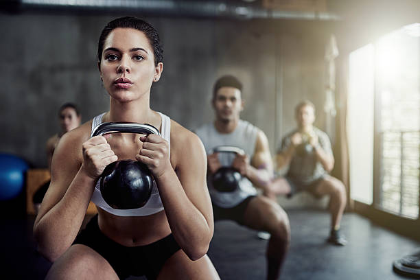 Burning calories and strengthening her core with a kettlebell Shot of a fit young woman working out with a kettle bell at the gym weight training stock pictures, royalty-free photos & images