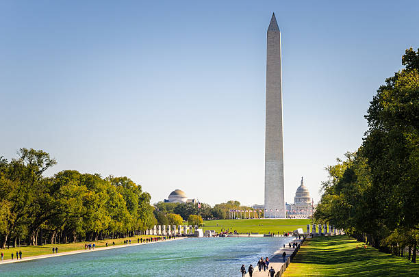 National Mall in Washington DC on a Clear Autumn Day Washington Monument on a Clear Autumn Day. There are People are walking along the pool in foreground while  the Congress is Visible in Background. national monument stock pictures, royalty-free photos & images