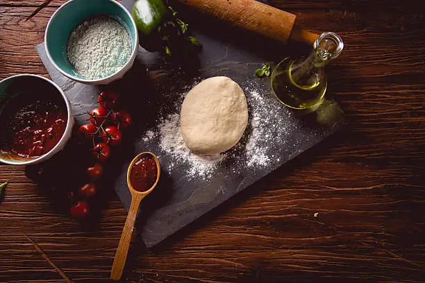 Photo of Dough with flour on wooden table, preparing homemade pizza