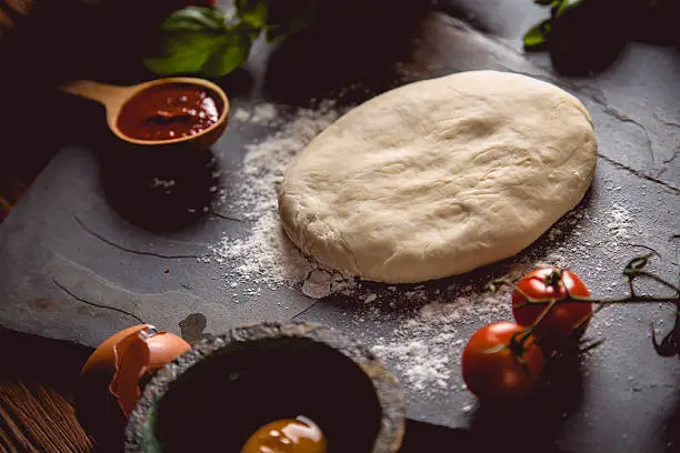 Photo of Dough with flour on wooden table, preparing homemade pizza