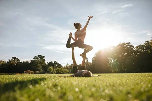 Healthy young couple doing acro yoga on grass. Man and woman doing various yoga poses in pair outdoors at the park.