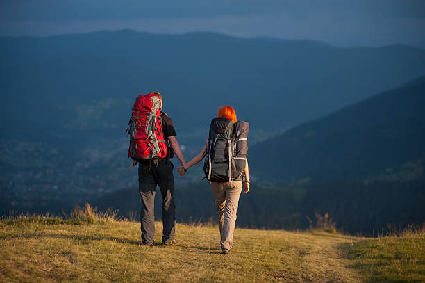 istock Hikers with backpacks holding hands and walking along a road 637786830