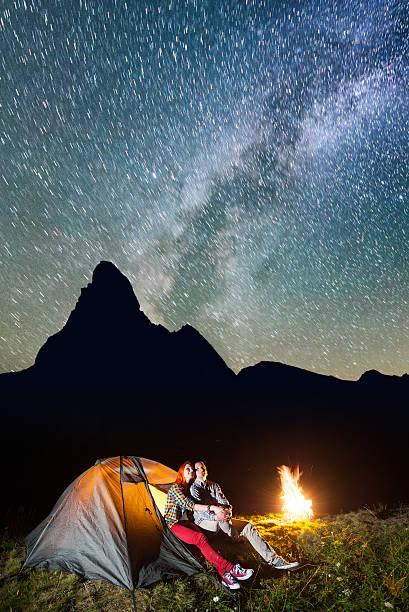 istock Romantic pair hikers sitting near glowing tent and campfire 637791946