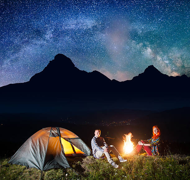 istock Pair tourists sitting by bonfire under incredibly beautiful starry sky 637797864