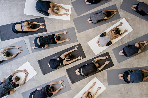 Child's Pose An aerial shot of a multi ethnic group of men and women practice yoga on on mats while wearing grey, black and white in an industrial setting. They are reaching forward in child's pose. community health center stock pictures, royalty-free photos & images