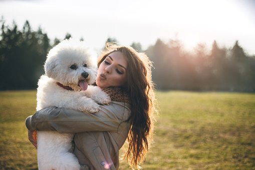 Beautiful young woman hugging her bichon frise dog in park