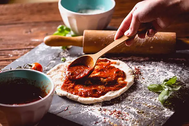 Photo of Girl is placing tomato sauce on fresh pizza