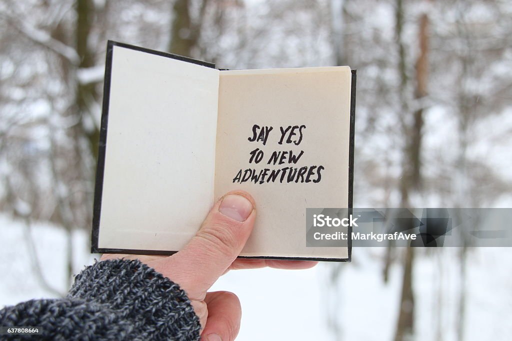 Male holding a book with the inscription Say yes to Hand holding a book with the inscription Say yes to new adventures on the background of the forest with snow-covered trees New Stock Photo